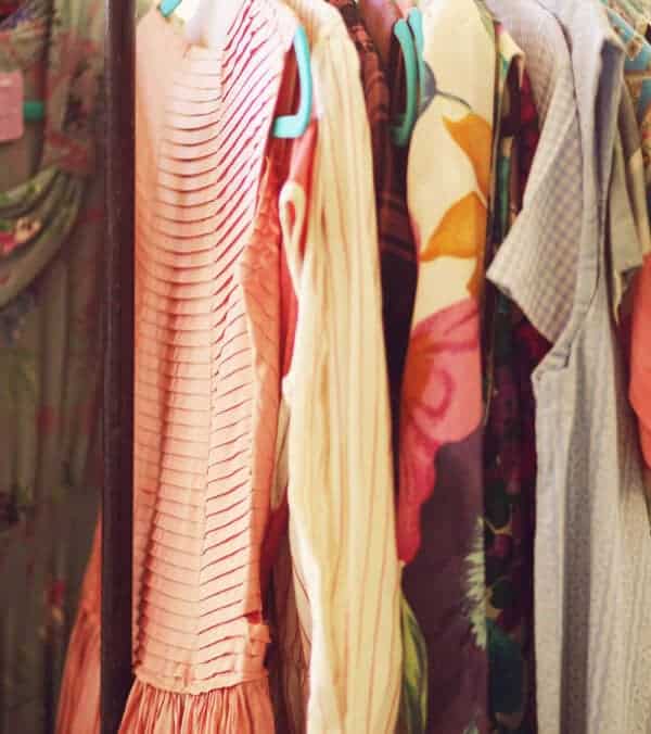 Several colorful garments, including a vintage sundress and a blue cotton dress, are beautifully displayed on hangers along the clothing rack.